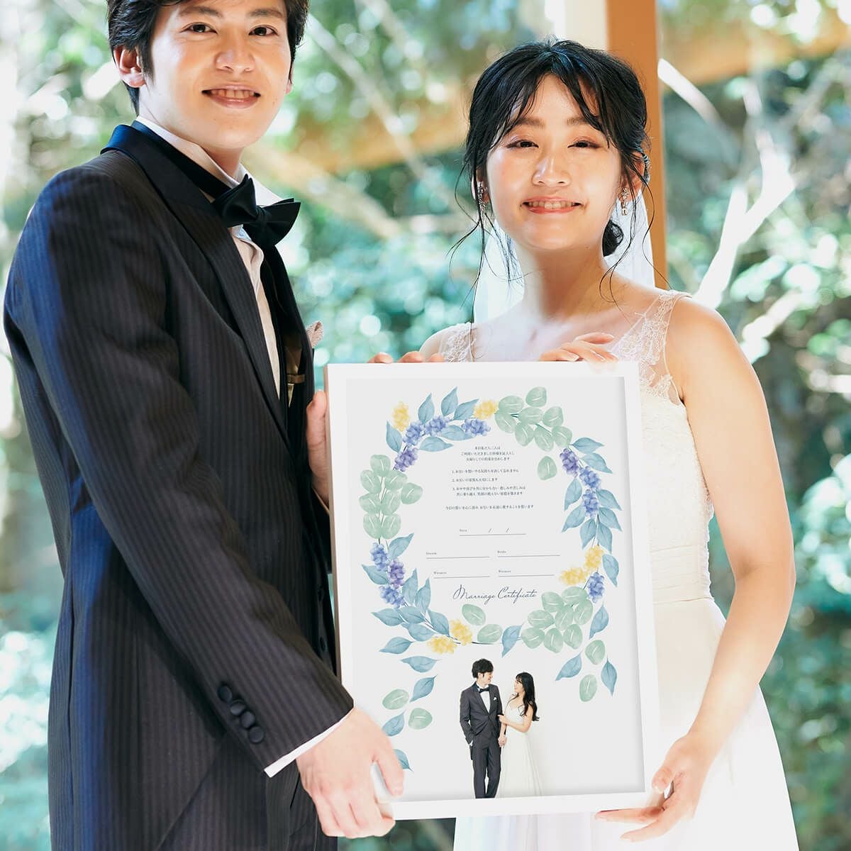 リースのイラスト写真入りゲスト参加型結婚証明書を掲げている新郎新婦