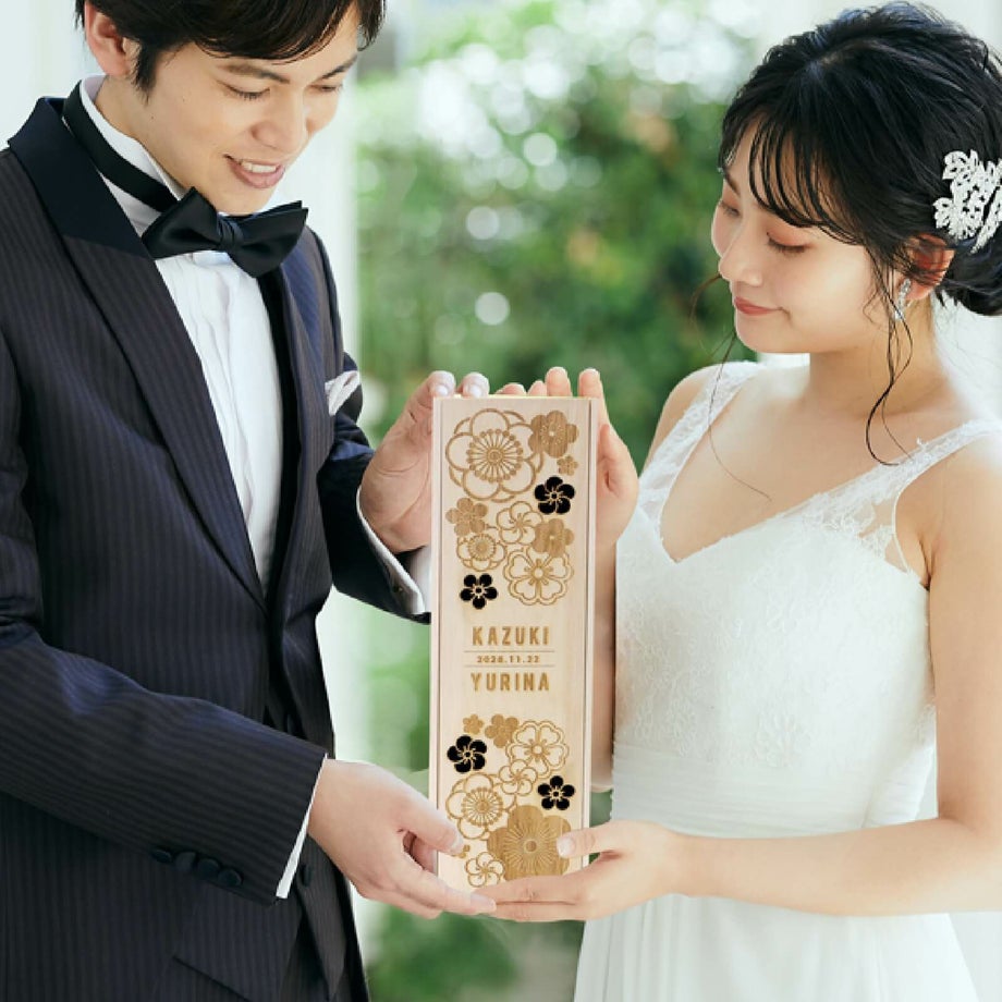 梅や桜などめでたい柄の木箱に日本酒が入ったギフトを持っている新郎新婦